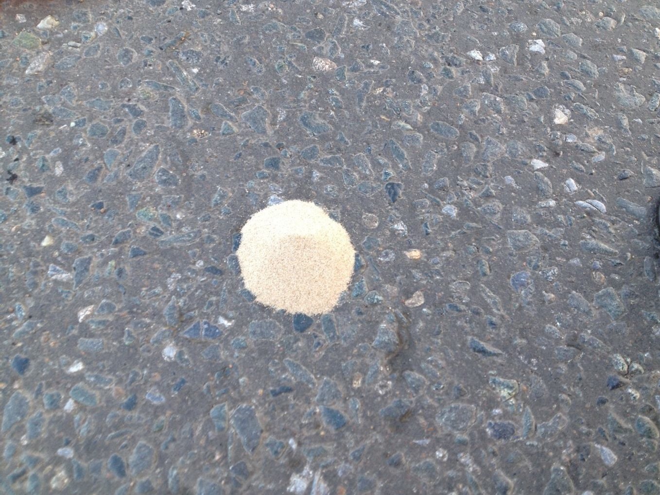 Песок, высыпанный из мерной емкости на асфальтобетонное покрытие